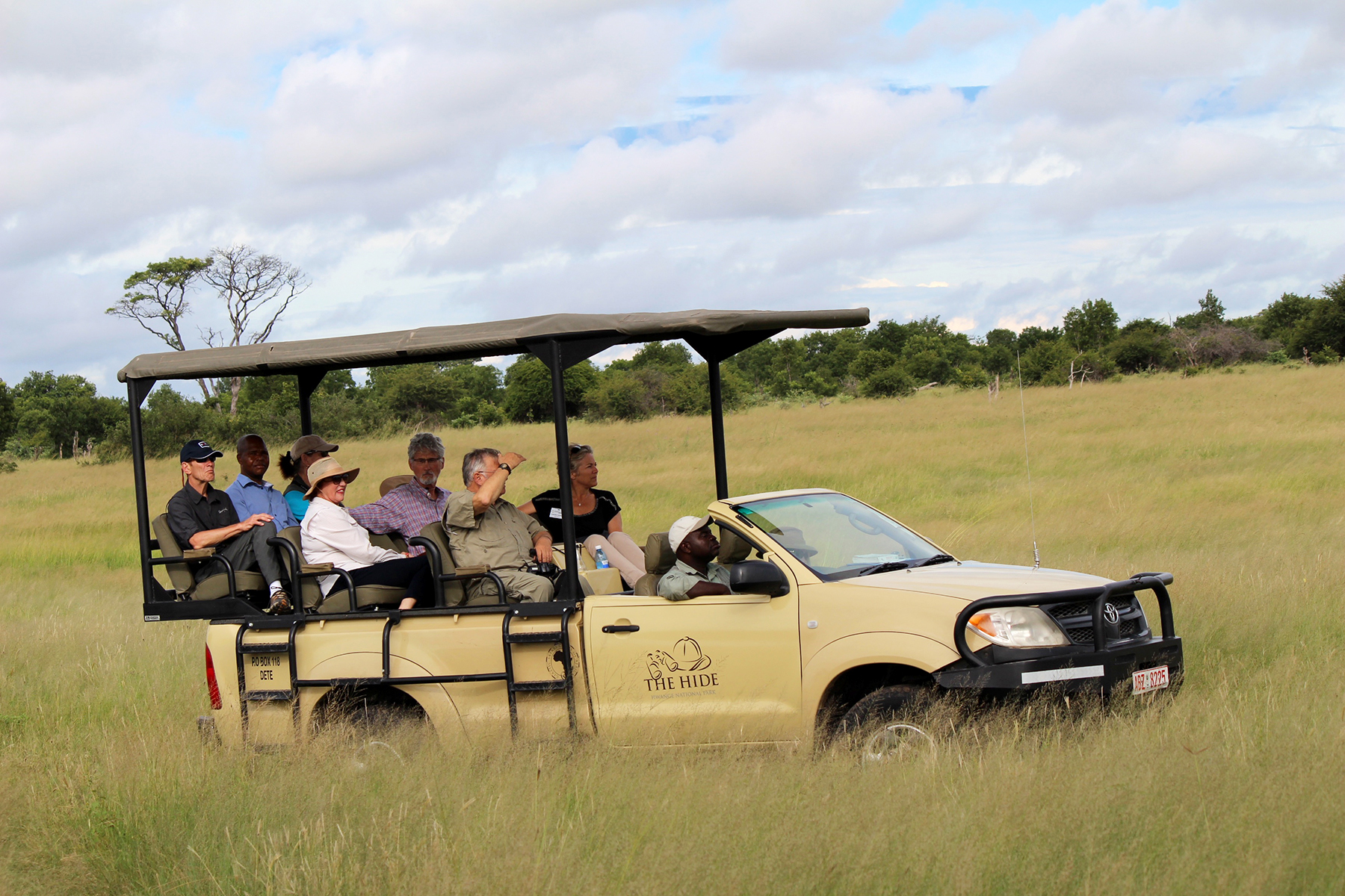 Safari vehicle carrying passengers through tall grass on a savanna.
