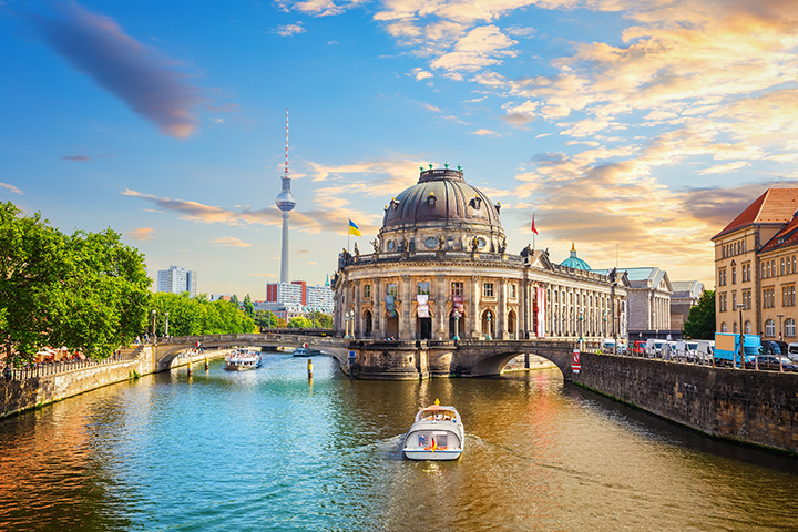 Riverside view in Berlin of a domed historic building with boats and city skyline.