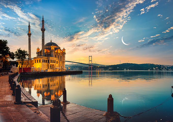 Ortaköy Mosque at dusk reflecting on the Bosphorus beneath a crescent moon.
