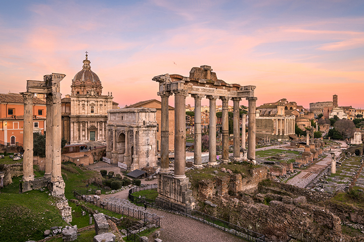 Ancient stone columns and ruins of the Roman Forum at sunset.