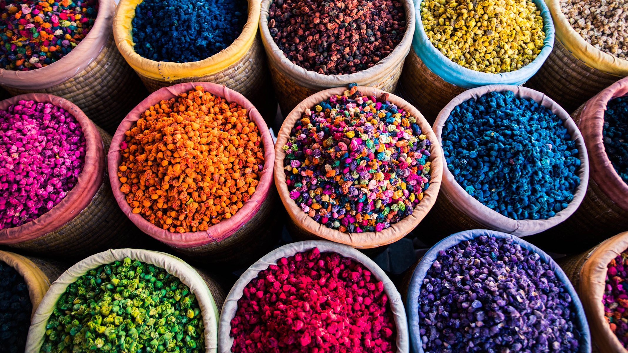 Vibrant, colorful baskets filled with various dried flowers in hues of pink, orange, yellow, blue, and purple, conveying a lively and aromatic market scene.