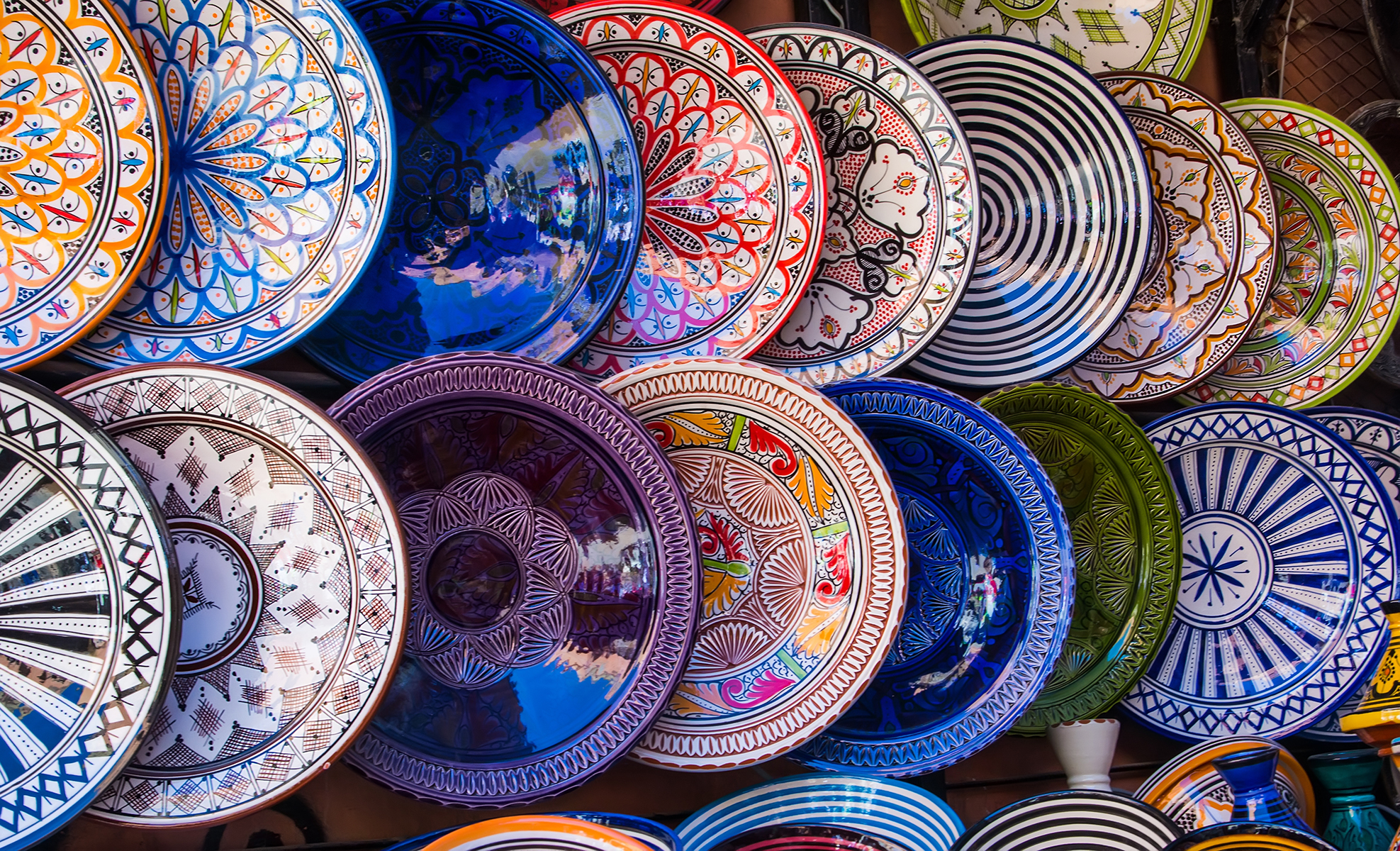 Vibrant ceramic plates displayed on a wall, featuring intricate patterns and bold colors like blue, red, and green, conveying a lively, artistic ambiance.