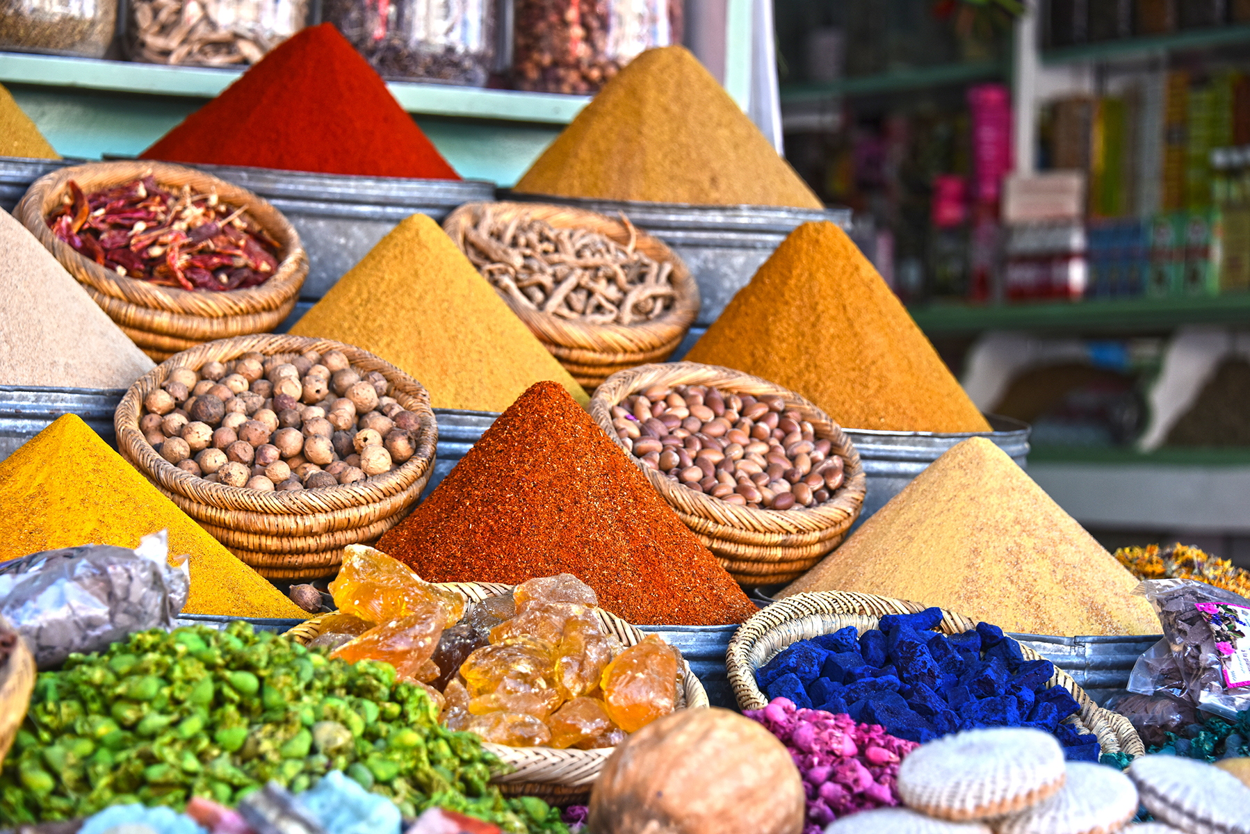Vibrant spice market display with colorful mounds of spices, nuts, and crystals in baskets. The diverse textures and hues create a lively, aromatic scene.