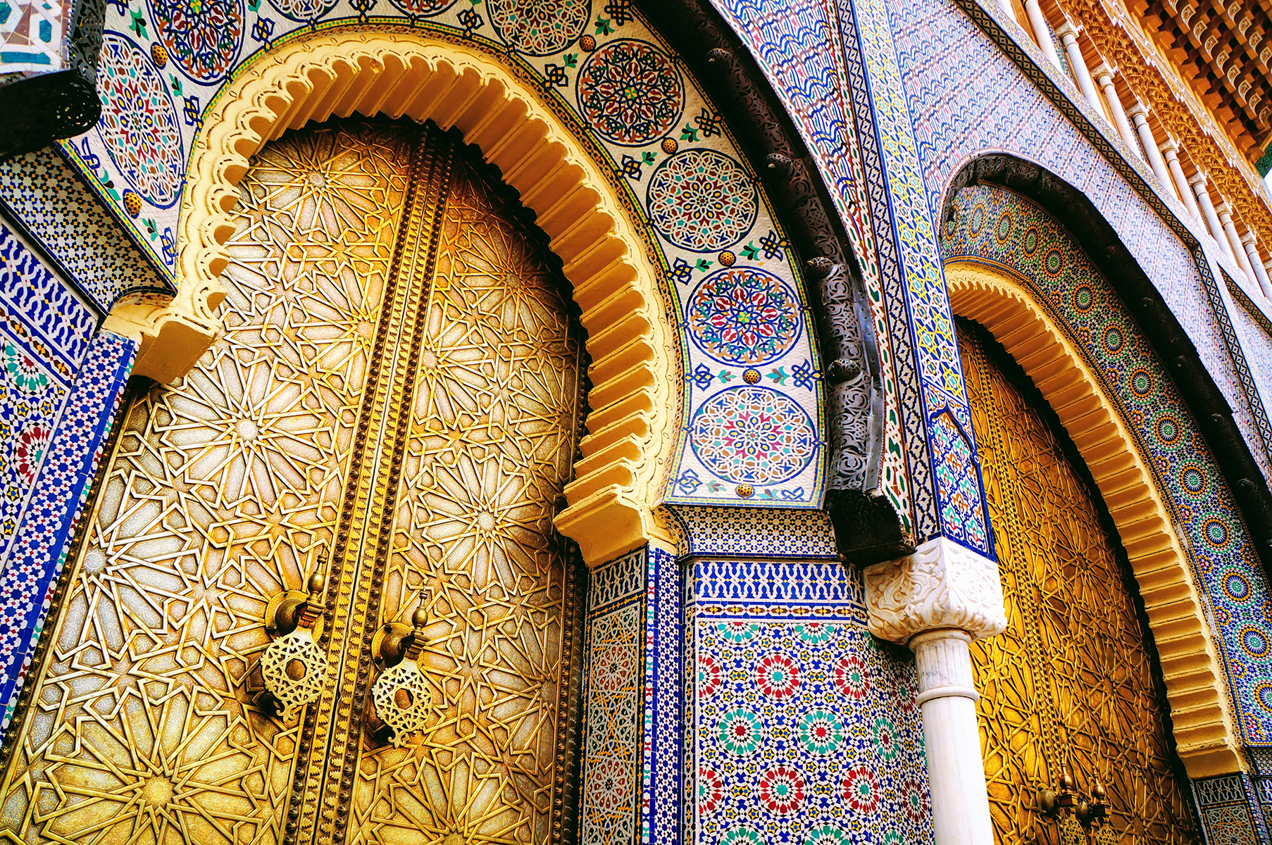 Ornate golden doors with intricate star patterns, framed by colorful, mosaic-tiled arches in traditional Moroccan style, exuding a rich, cultural elegance.