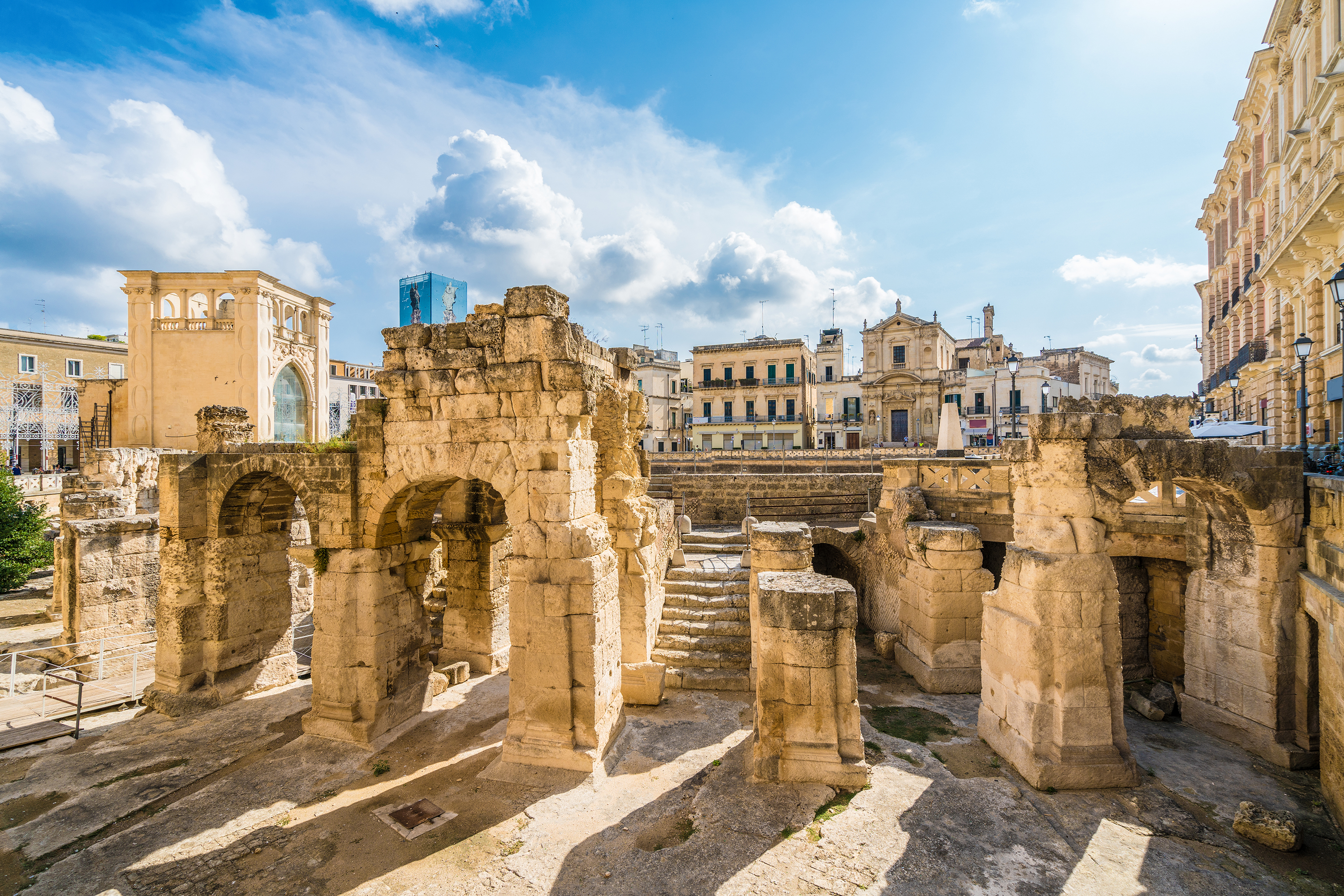 Roman amphitheater ruins in Lecce set among surrounding historic city buildings.