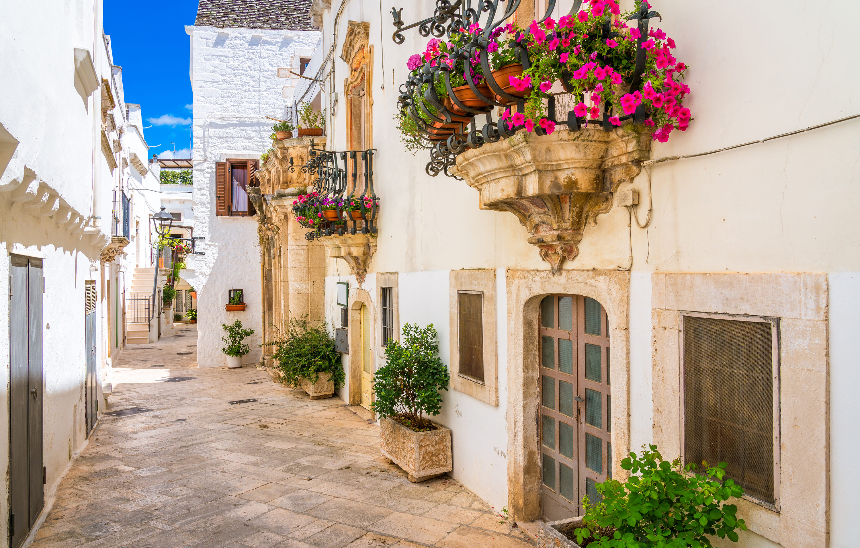 Quiet alley in Locorotondo featuring whitewashed buildings and flower-filled balconies.