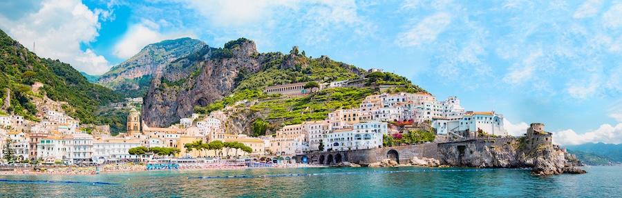 Panoramic aerial view of the small harbor village of Amalfi on the Amalfi Coast, Salerno, Campania, Italy, showcasing colorful houses perched on rocky cliffs and a tiny beach along the sparkling sea.