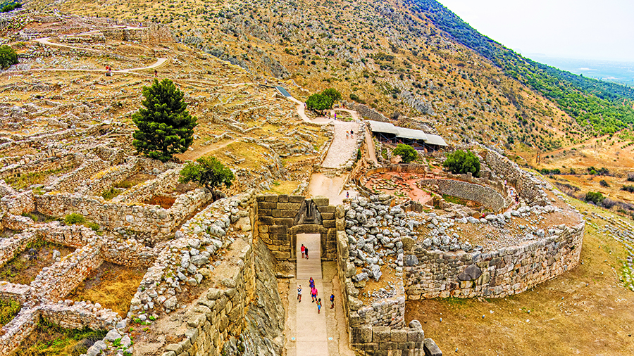 Ancient stone ruins on a hillside with a walkway leading through large walls and rocky terrain.