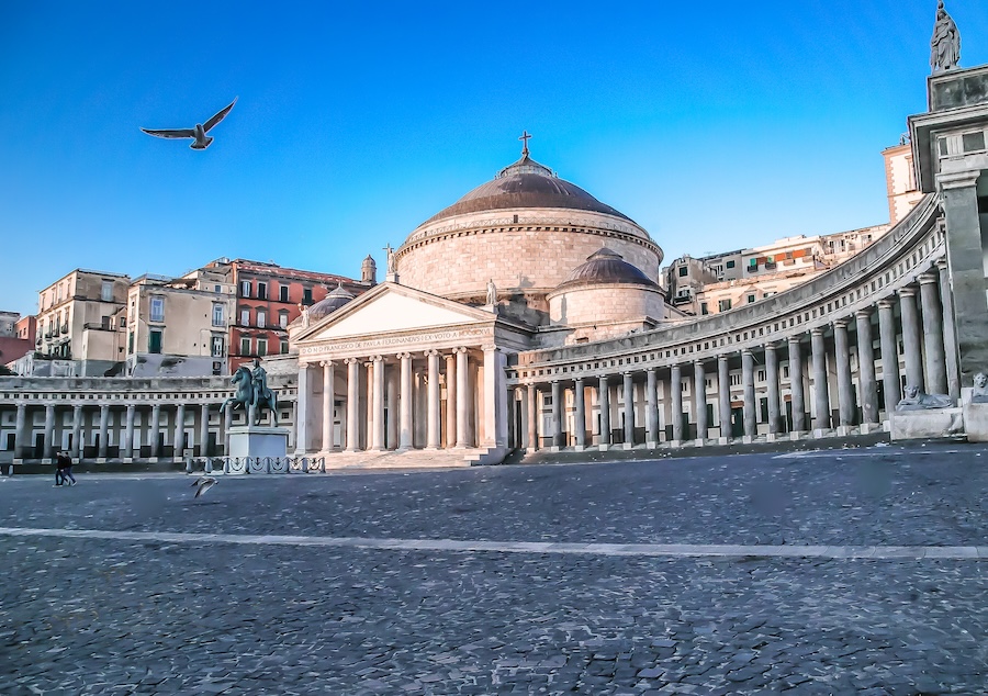 Wide view of Piazza del Plebiscito, the grand public square in Naples, Italy, framed by historic buildings under a clear sky.