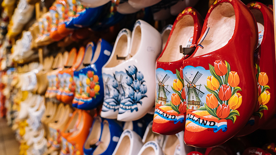 A colorful display of traditional wooden clogs in a shop. The clogs feature vibrant painted tulips and windmills, conveying a cheerful, cultural vibe.