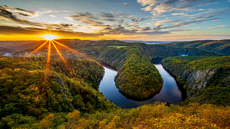 Aerial view of the Vltava River surrounded by green trees.