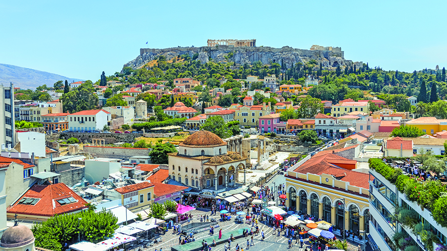 A scenic view of a historic city with red‑roofed buildings, a busy square, and an ancient hilltop fortress in the background.