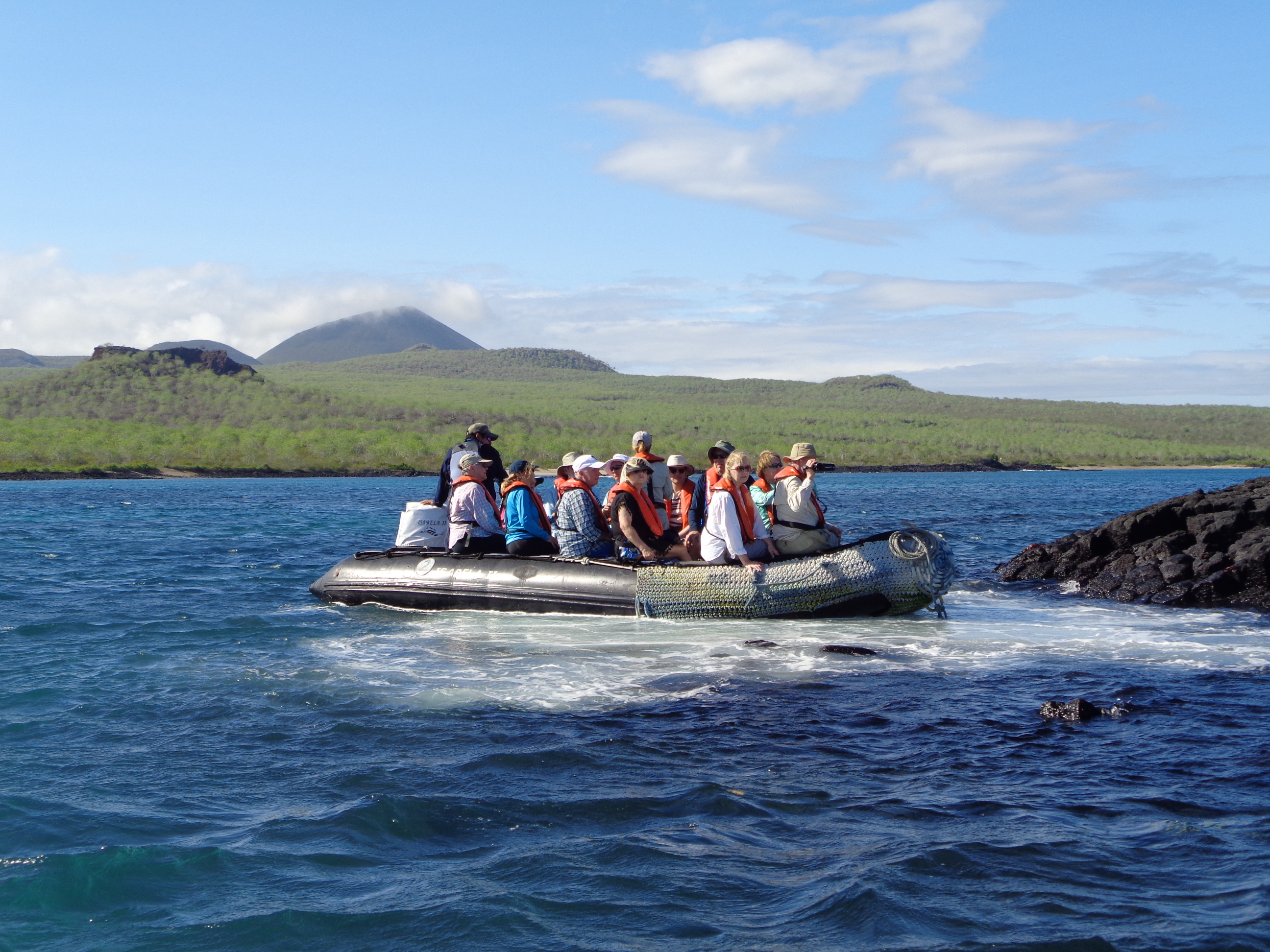 A small boat full of people wearing life jackets traveling on the ocean near rocky shorelines.