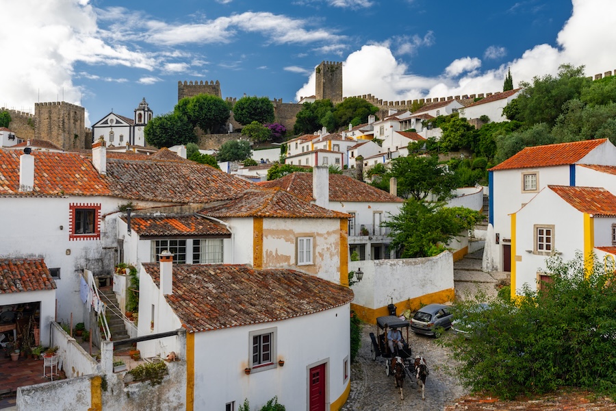 The medieval town of Óbidos, Portugal, with whitewashed houses, terracotta roofs, cobbled streets, and a castle atop a hill.