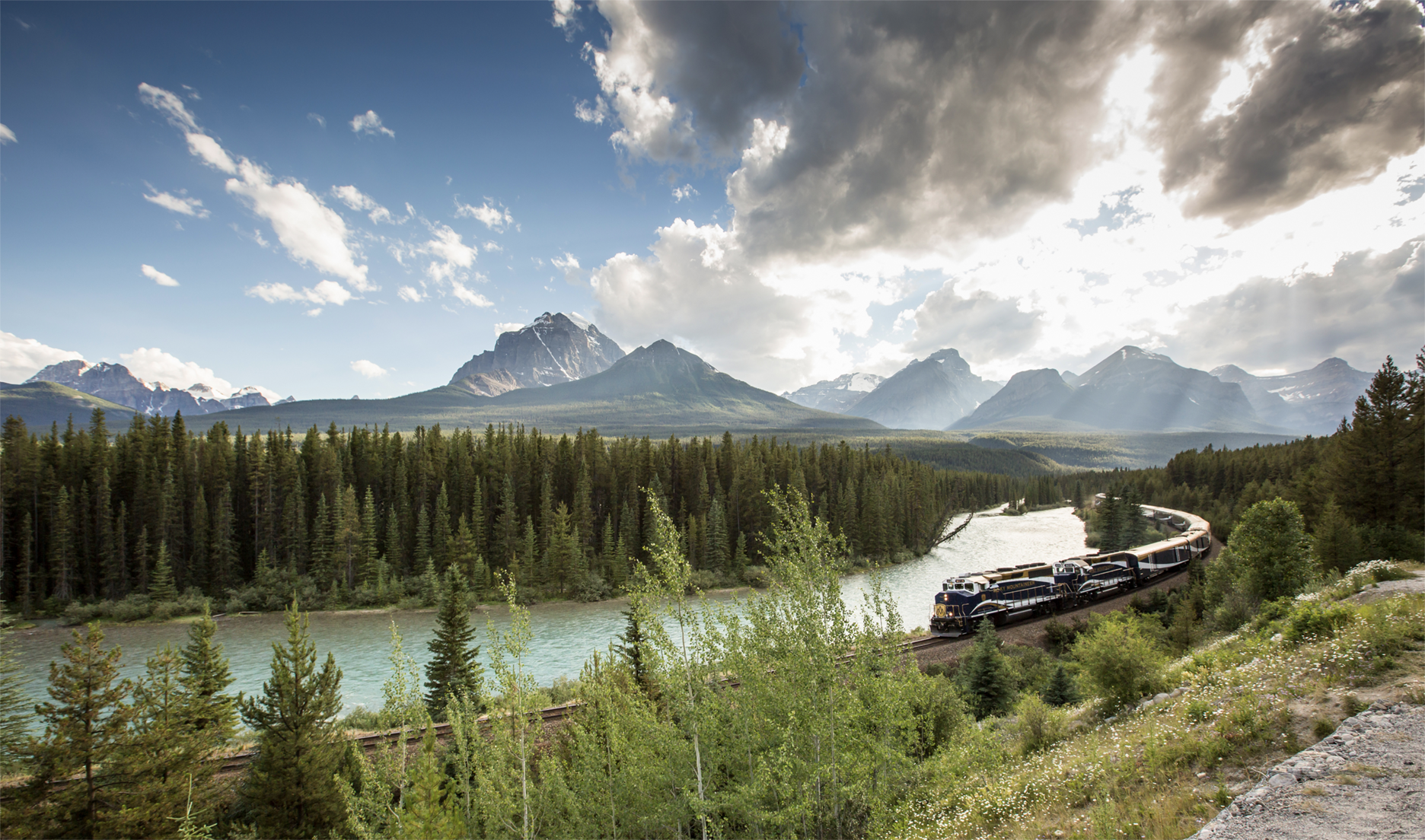 The Rocky Mountaineer train traveling beside the Bow River through forested valleys in the Rockies.