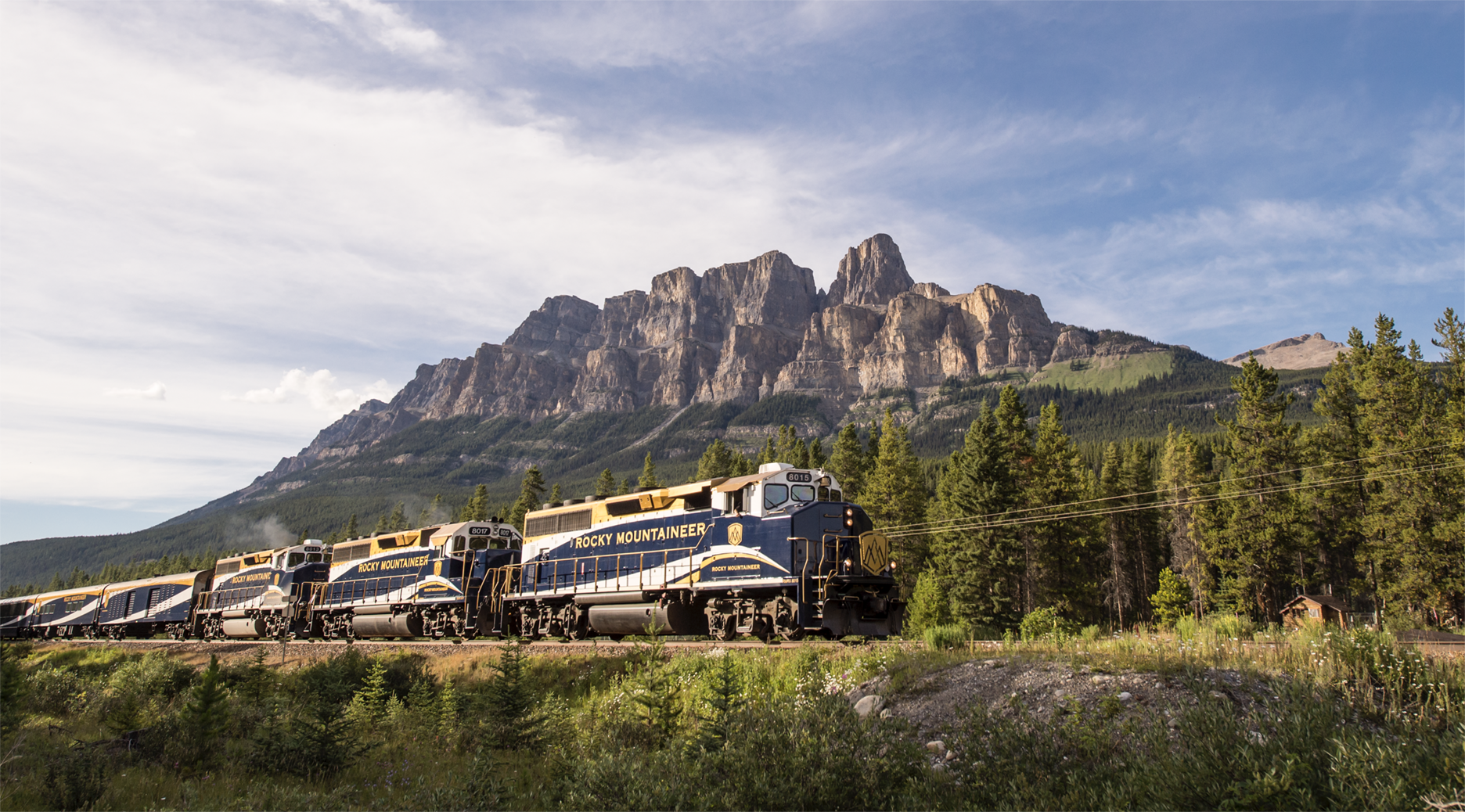 The Rocky Mountaineer train passing through alpine wilderness with Castle Mountain rising in the background.