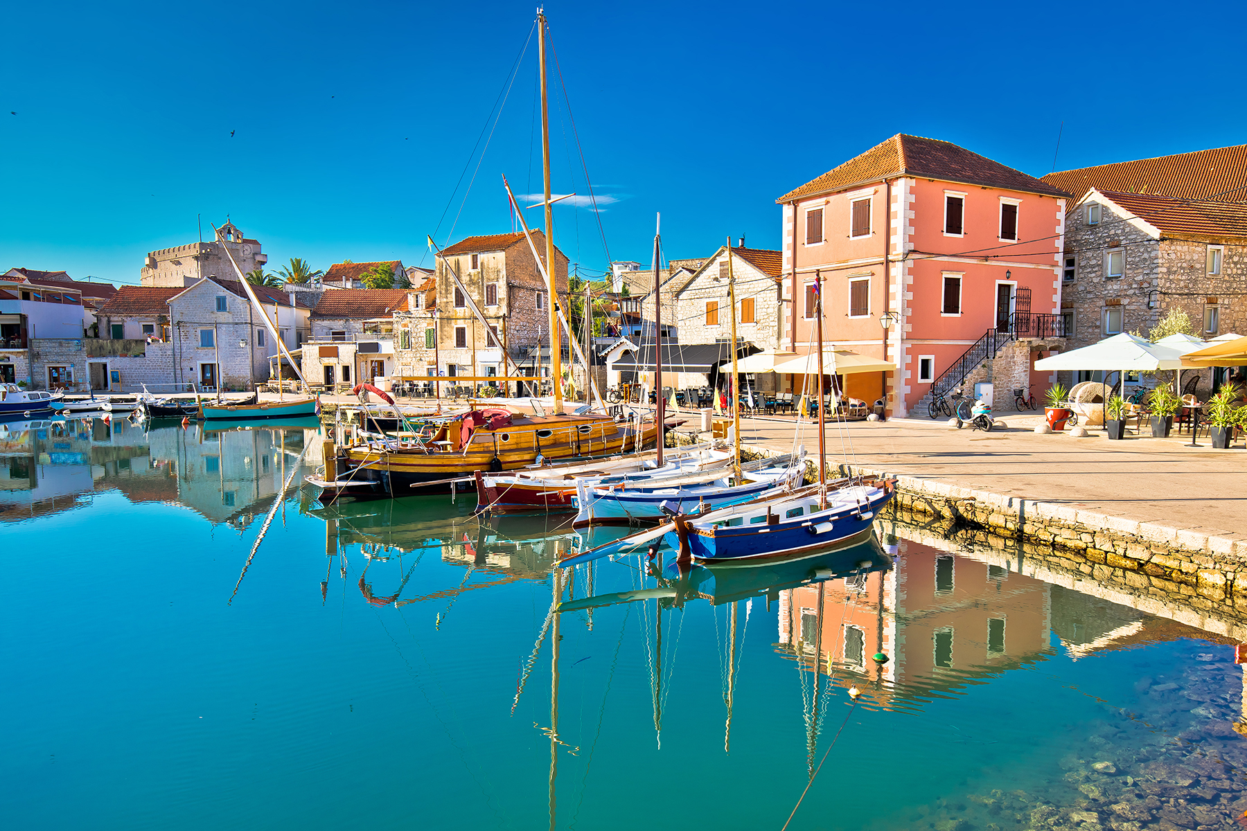 A picturesque harbor with colorful boats reflecting on tranquil waters, surrounded by charming old stone buildings and a clear blue sky.