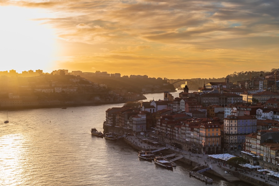 Scenic sunset over Ribeira district in Porto, Portugal, with Douro River, colorful buildings, and boats.