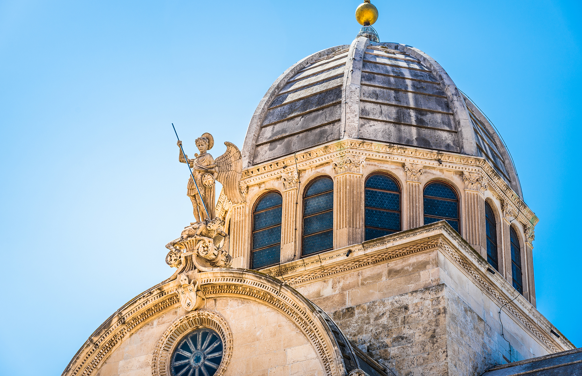 A detailed view of a domed structure topped with a golden orb and an ornate figure, set against a clear blue sky.