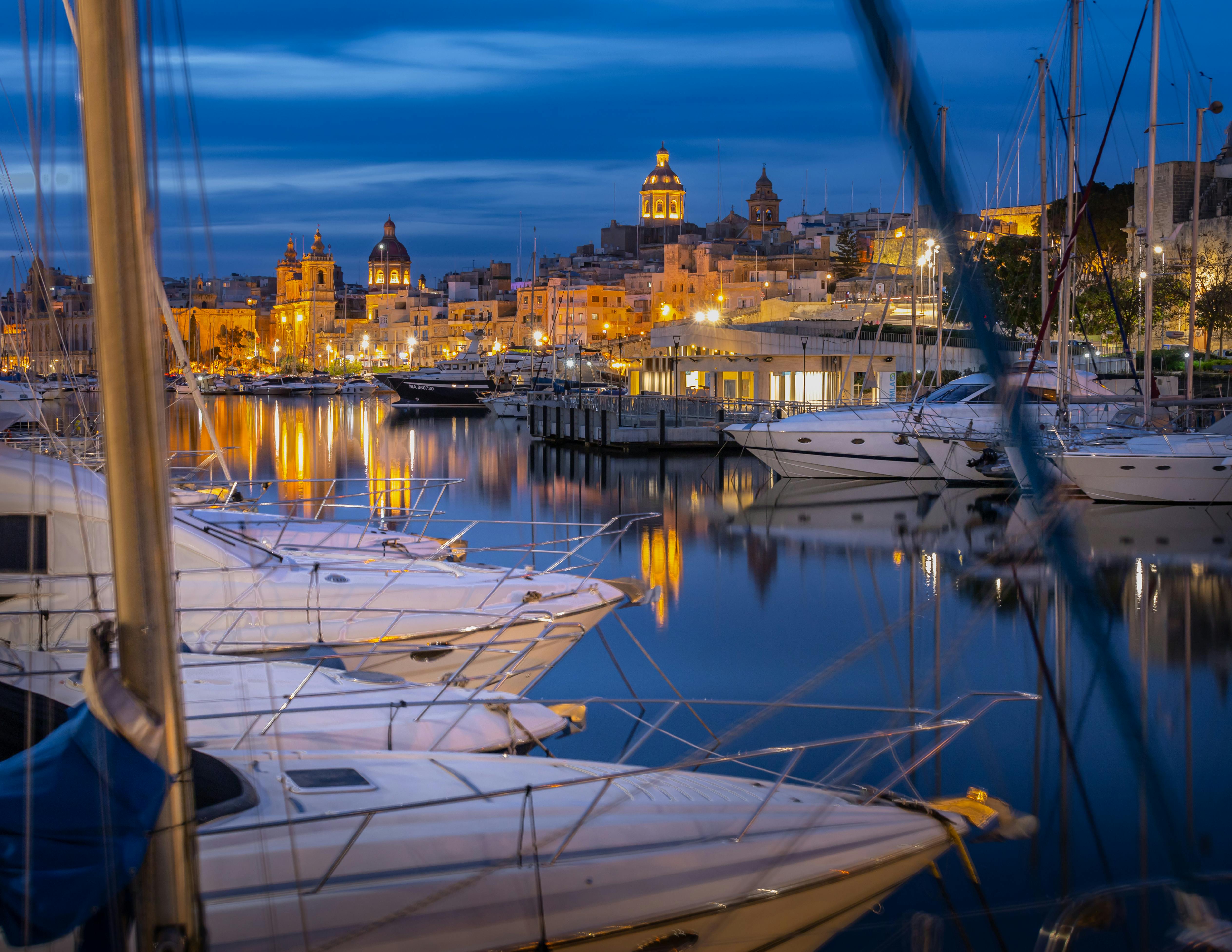 Night view of Valletta marina with yachts and illuminated city skyline.