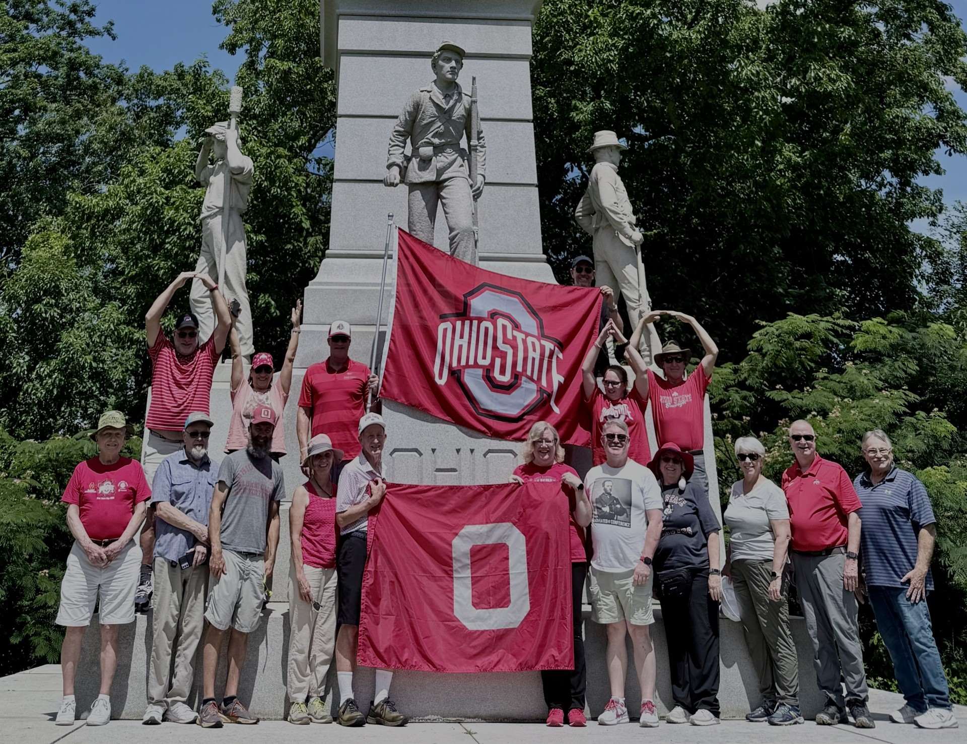 Group of alumni holding Ohio State flags and posing with statues.