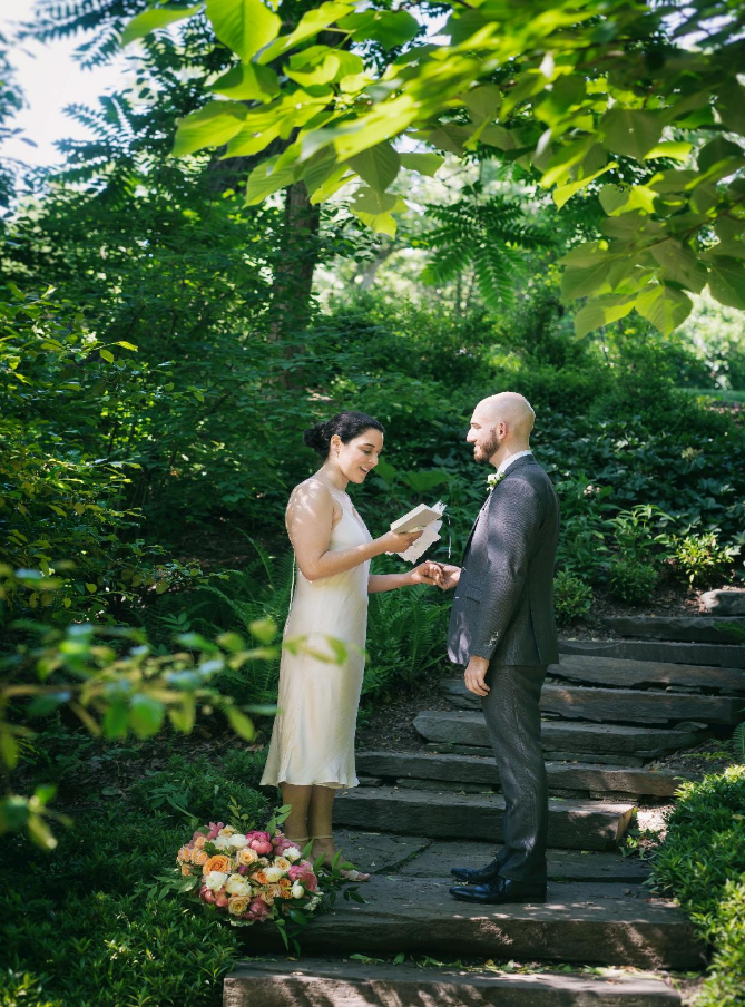 Mary and Niko at their wedding, giving their vows on stone steps, with greenery and stone steps behind them