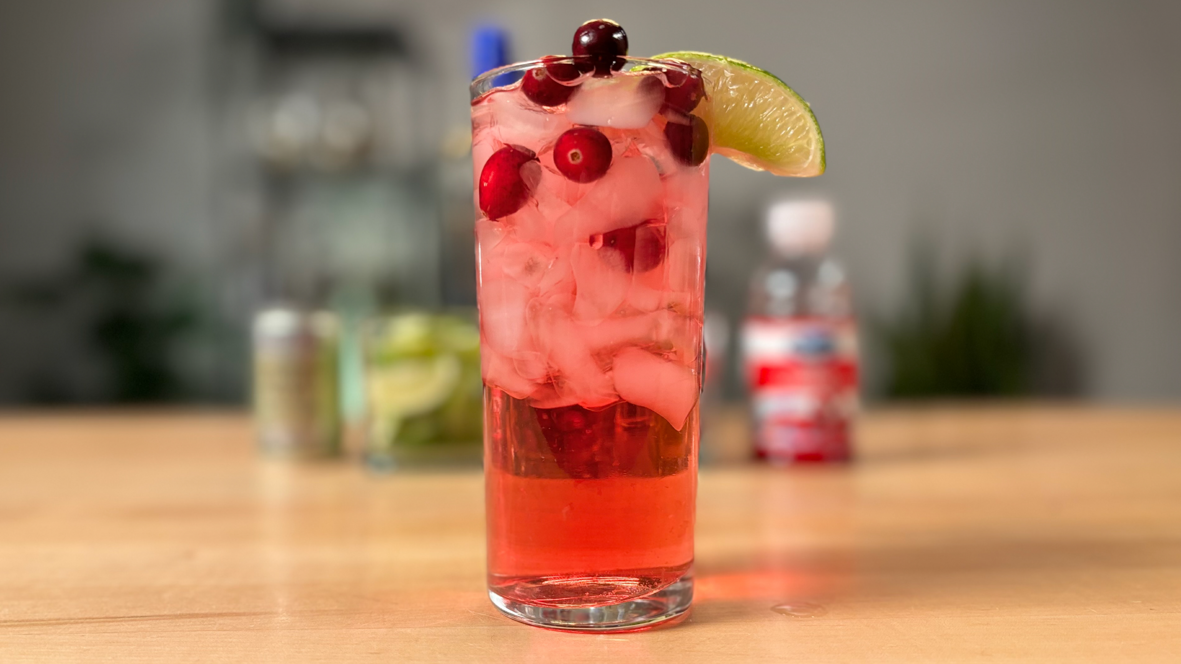 the scarlet spritzer drink is red with ice, cranberries and a slice of lime