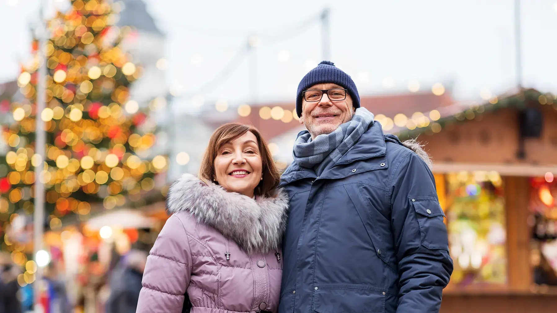 Man and woman posing at holiday market in front of decorated tree