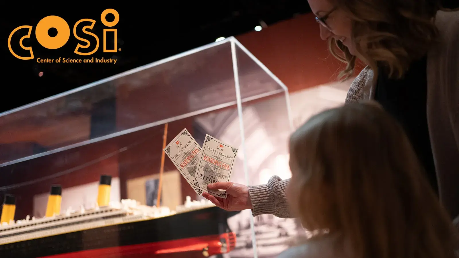 A woman showing a little girl two boarding tickets to Titanic with the COSI logo