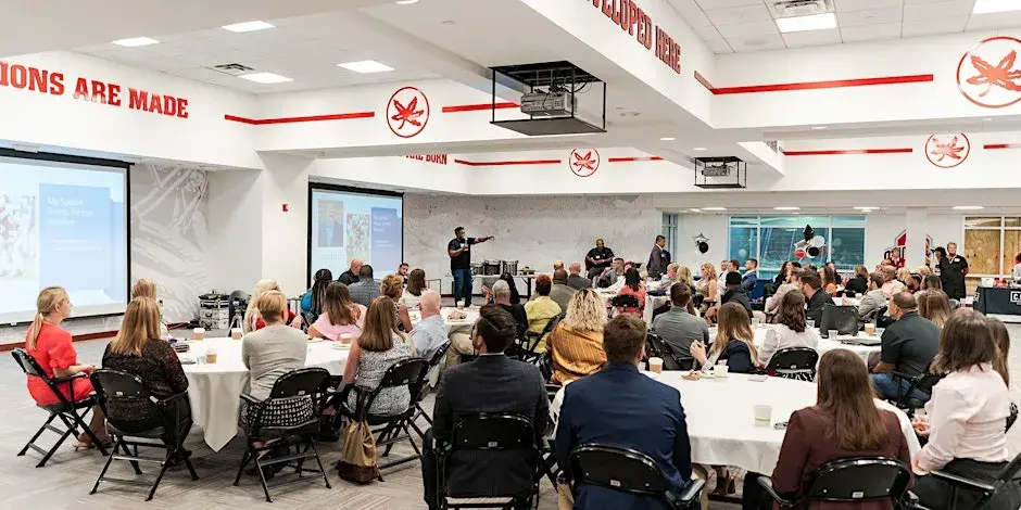 attendees sit at tables while speaker stands at front
