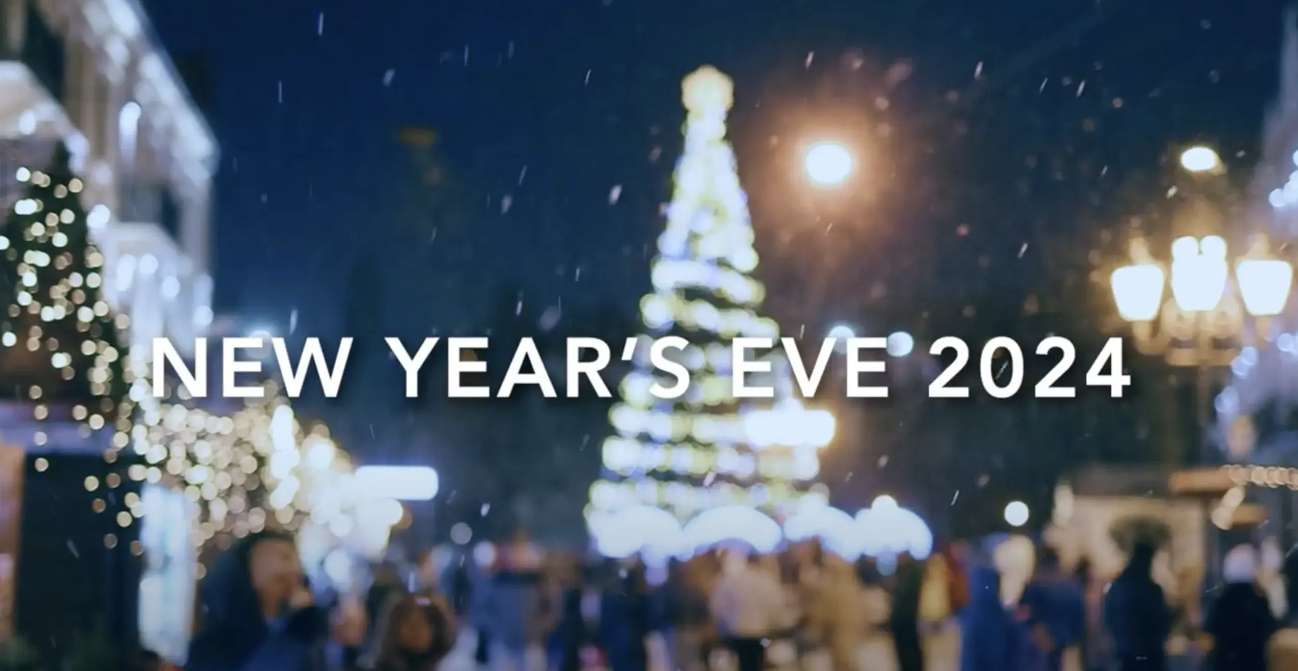 Christmas tree lit up outside in a small town at night with text reading New Year's Eve 2024