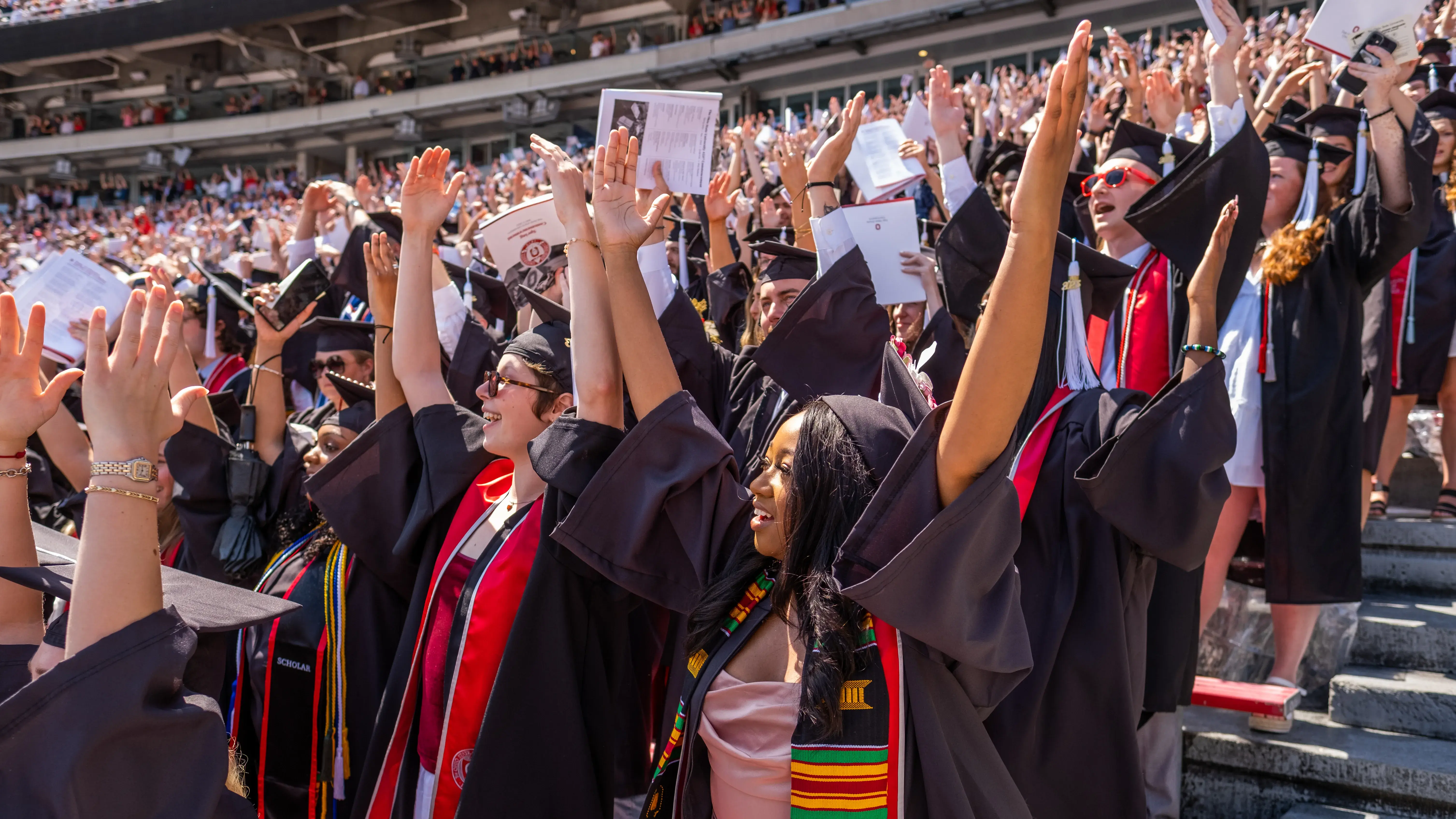 students in cap and gown raise their arms in the air at graduation
