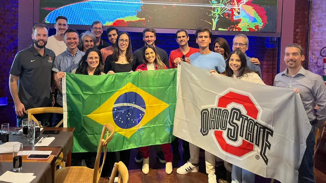 ohio state alumni posing for a photo holding a flag of brazil and an ohio state flag