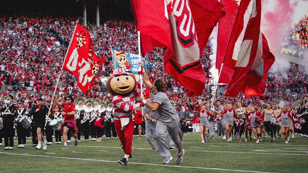 brutus buckeye leads the team onto the field holding red ohio state flags