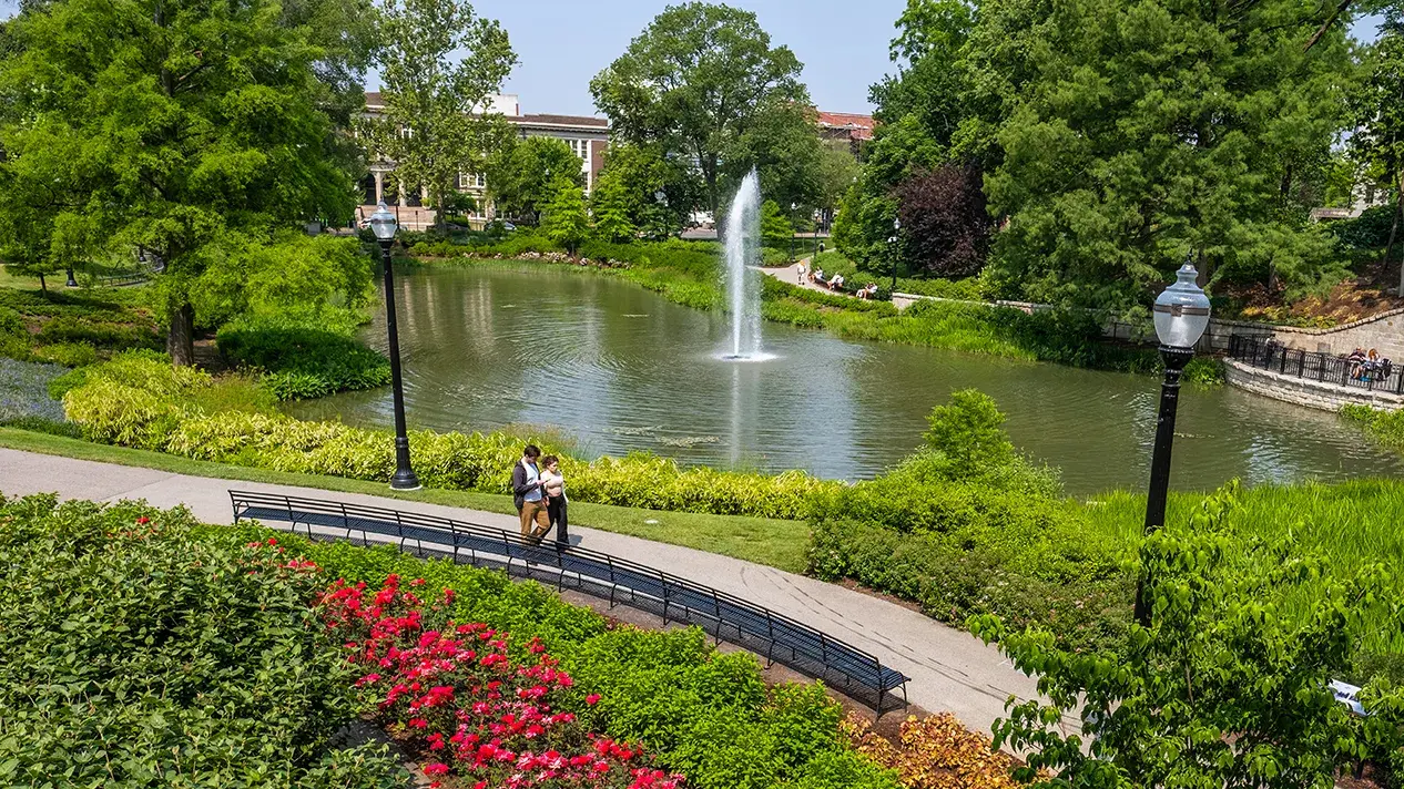 fountain in mirror lake in the spring surrounded by red flowers and green bushes