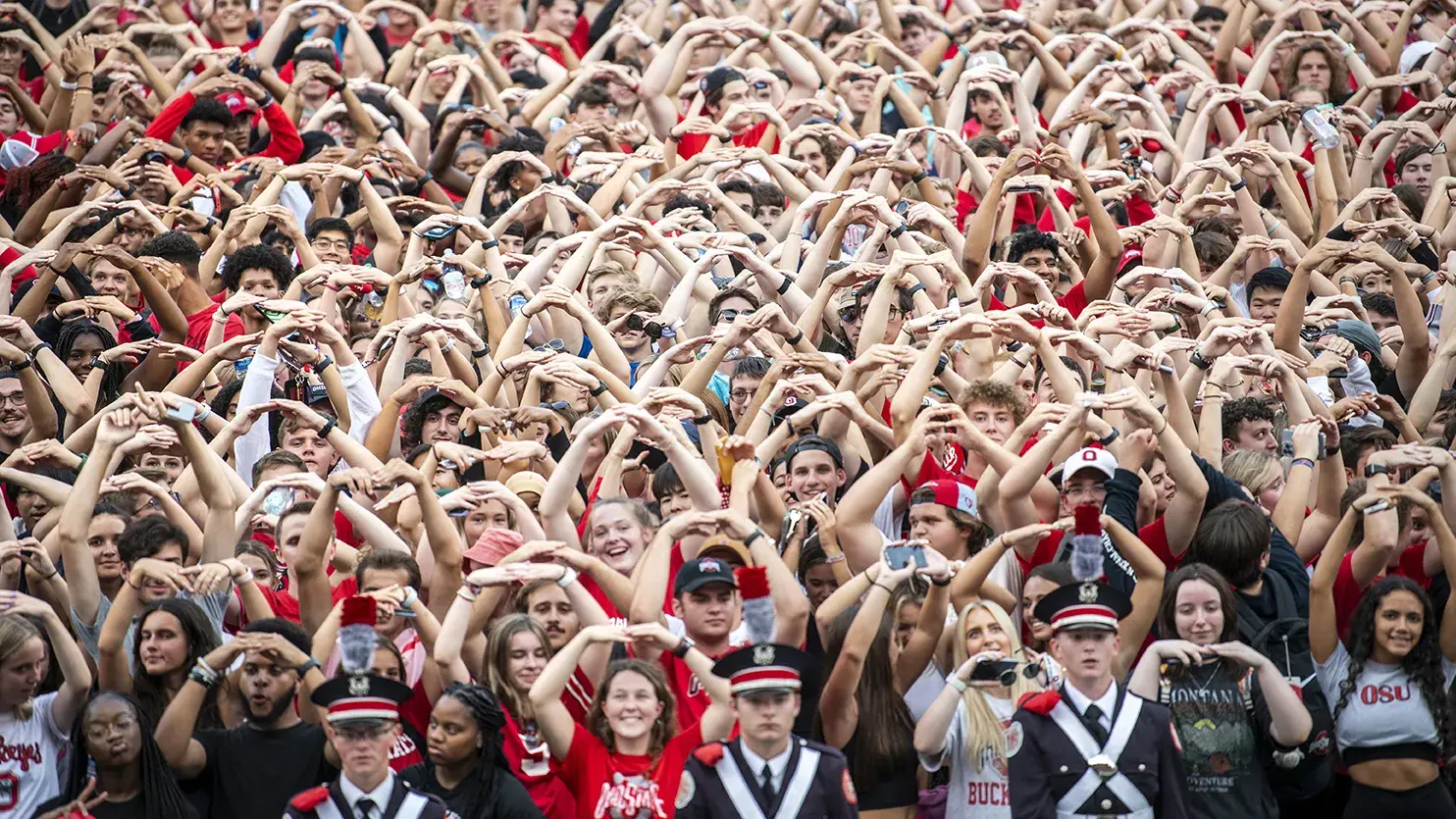 hundreds of OSU fans in a stadium raising their arms to form an O