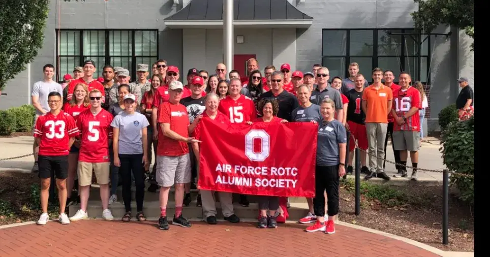 ohio state alumni group poses for a photo holding a red osu banner outdoors