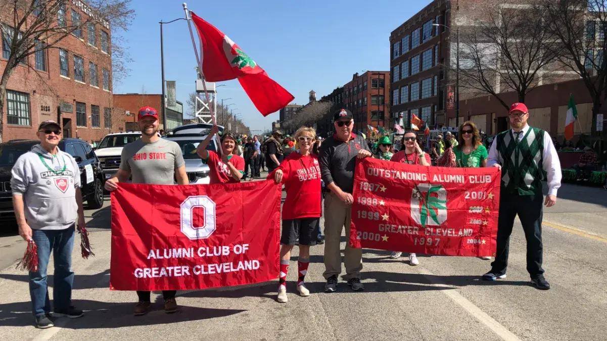 ohio state alumni holding osu banners and flags walking in a parade in cleveland