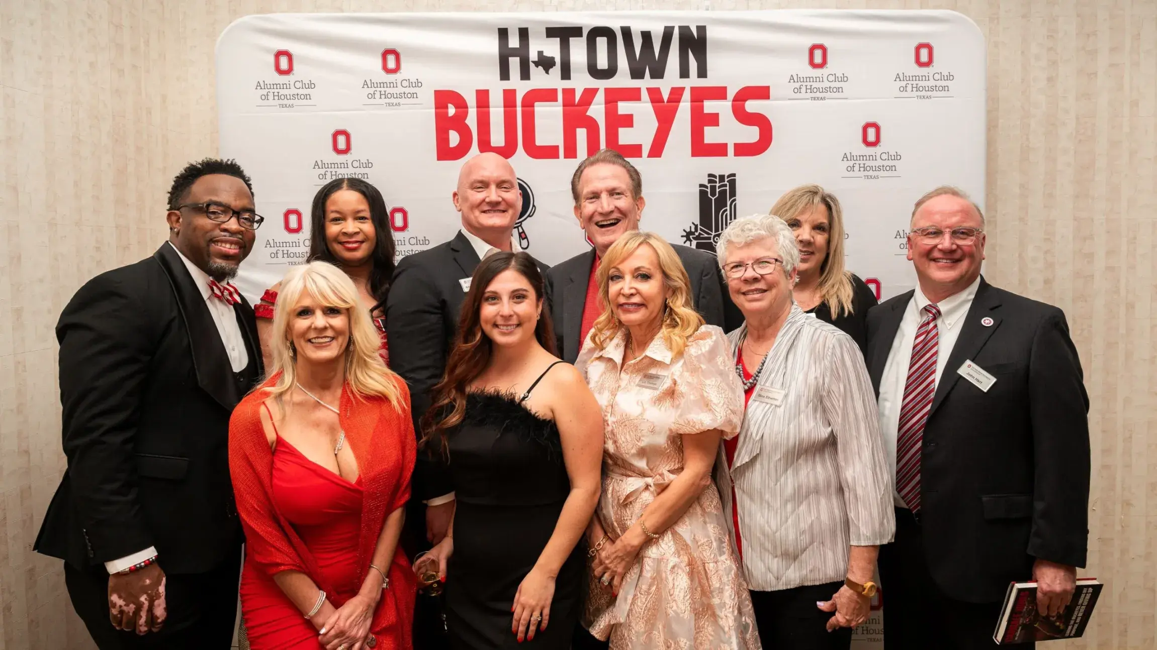 ohio state alumni in semi-formal attire posing for a photo in front of an H-Town Buckeys banner