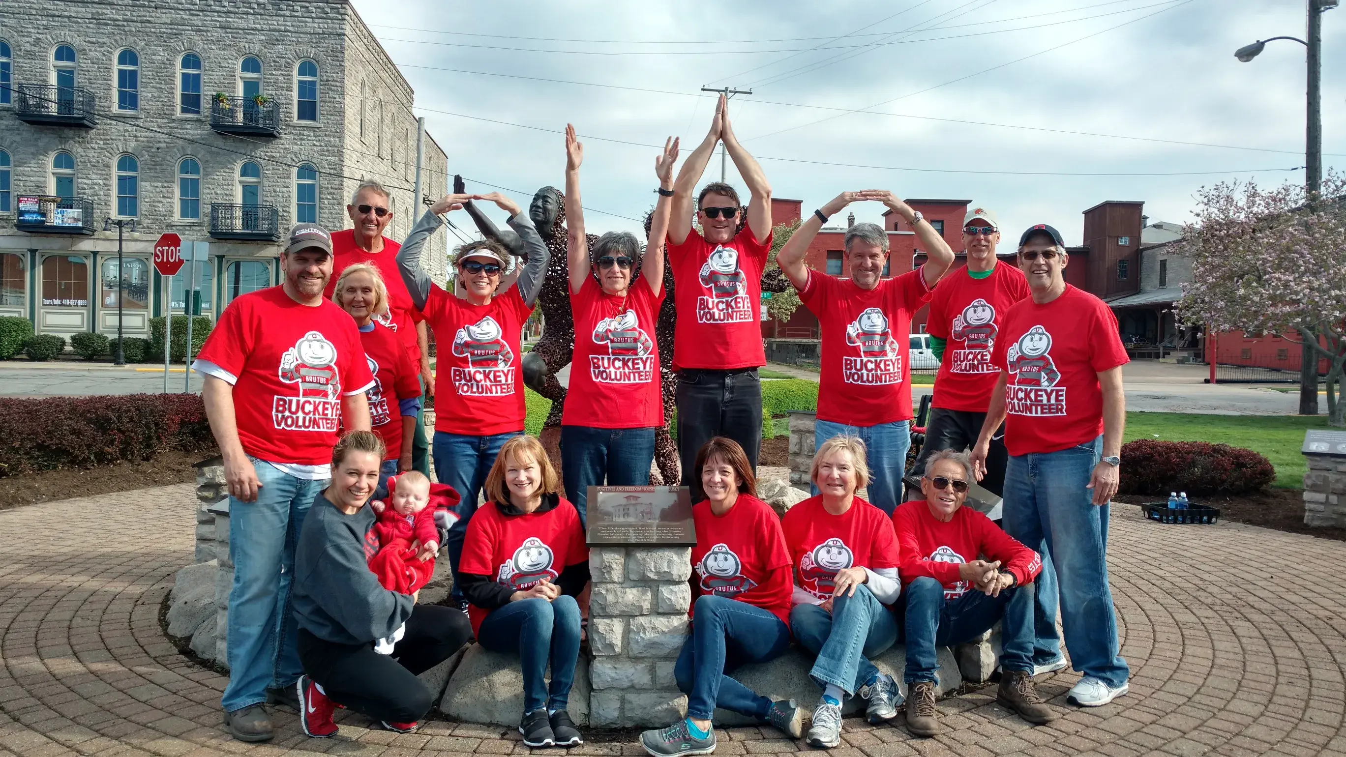 ohio state alumni posing for a photo outdoors with their arms in the air forming O H I O