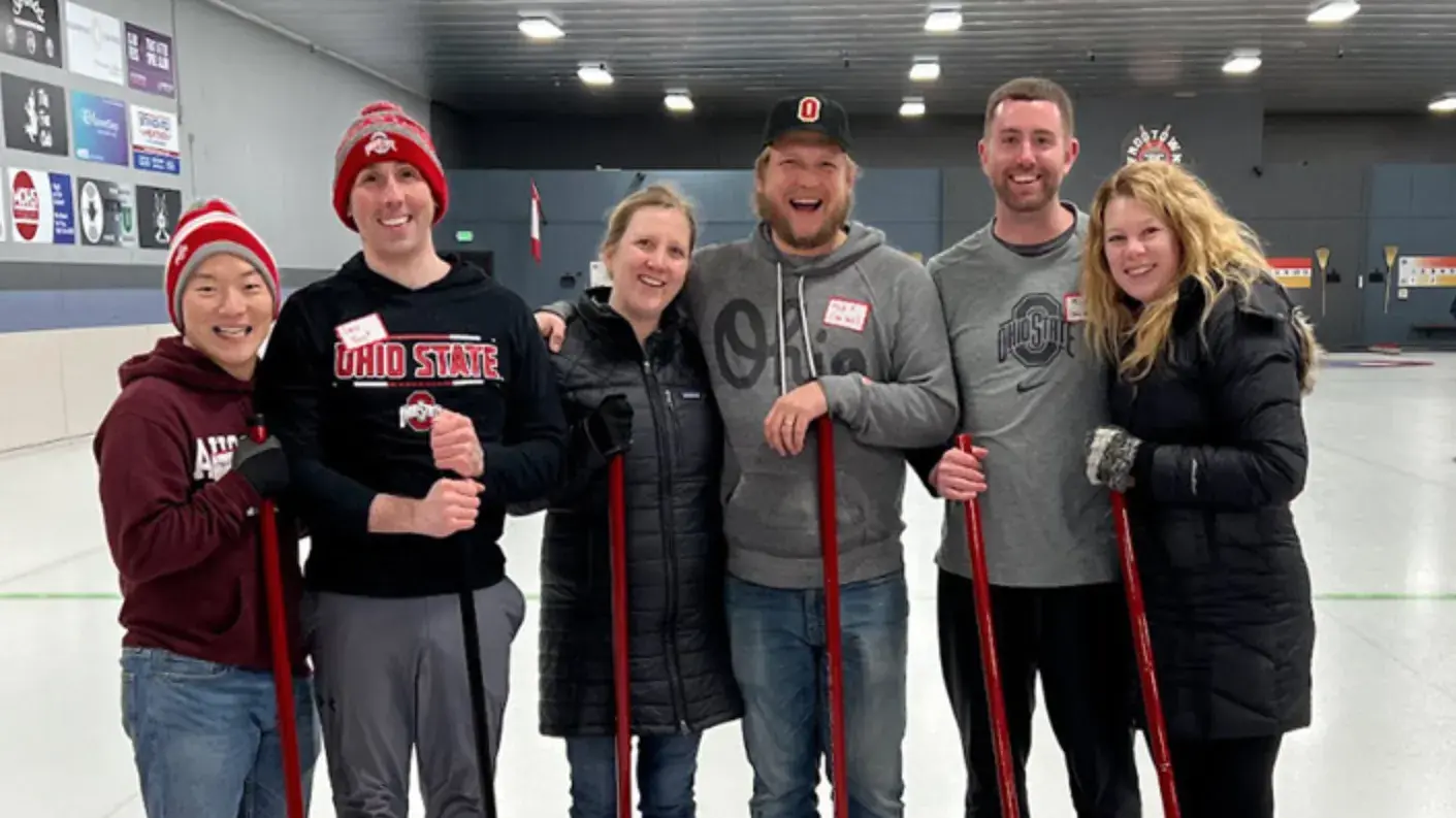 six ohio state alumni posing for a photo in an ice rink wearing warm ohio state gear 