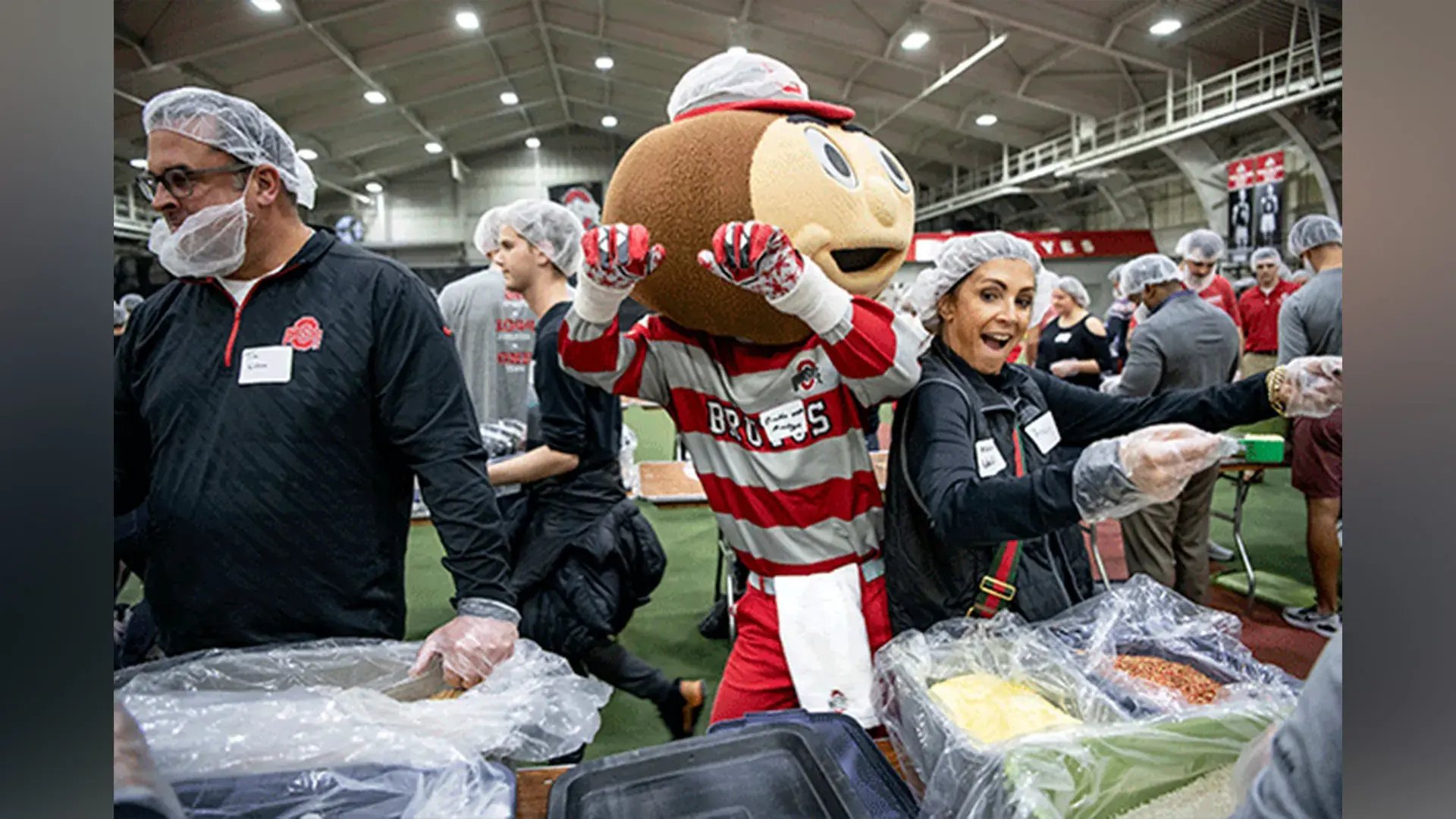 Brutus dances with volunteers wearing hairnets and packing meals