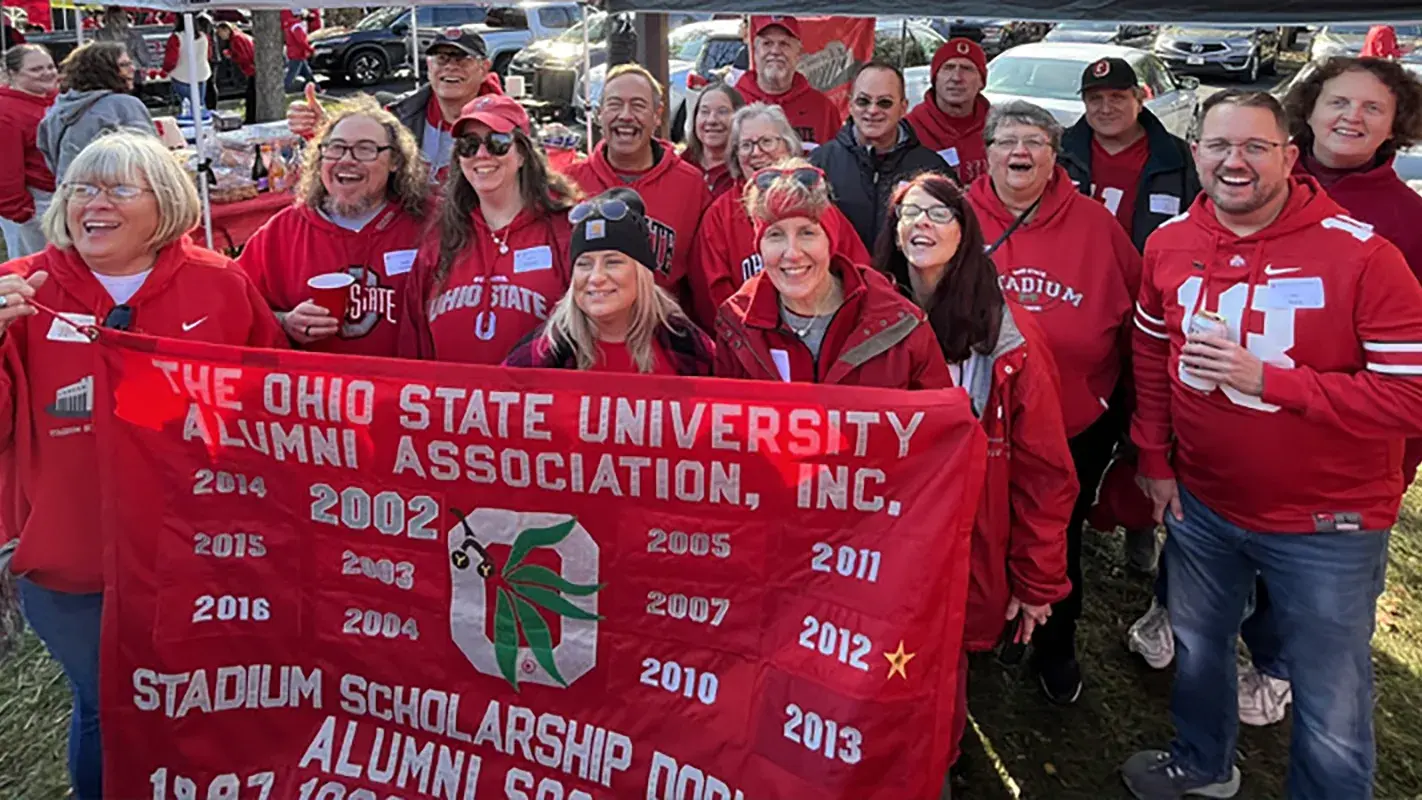 group of ohio state alumni holding an osu banner at an outdoor event