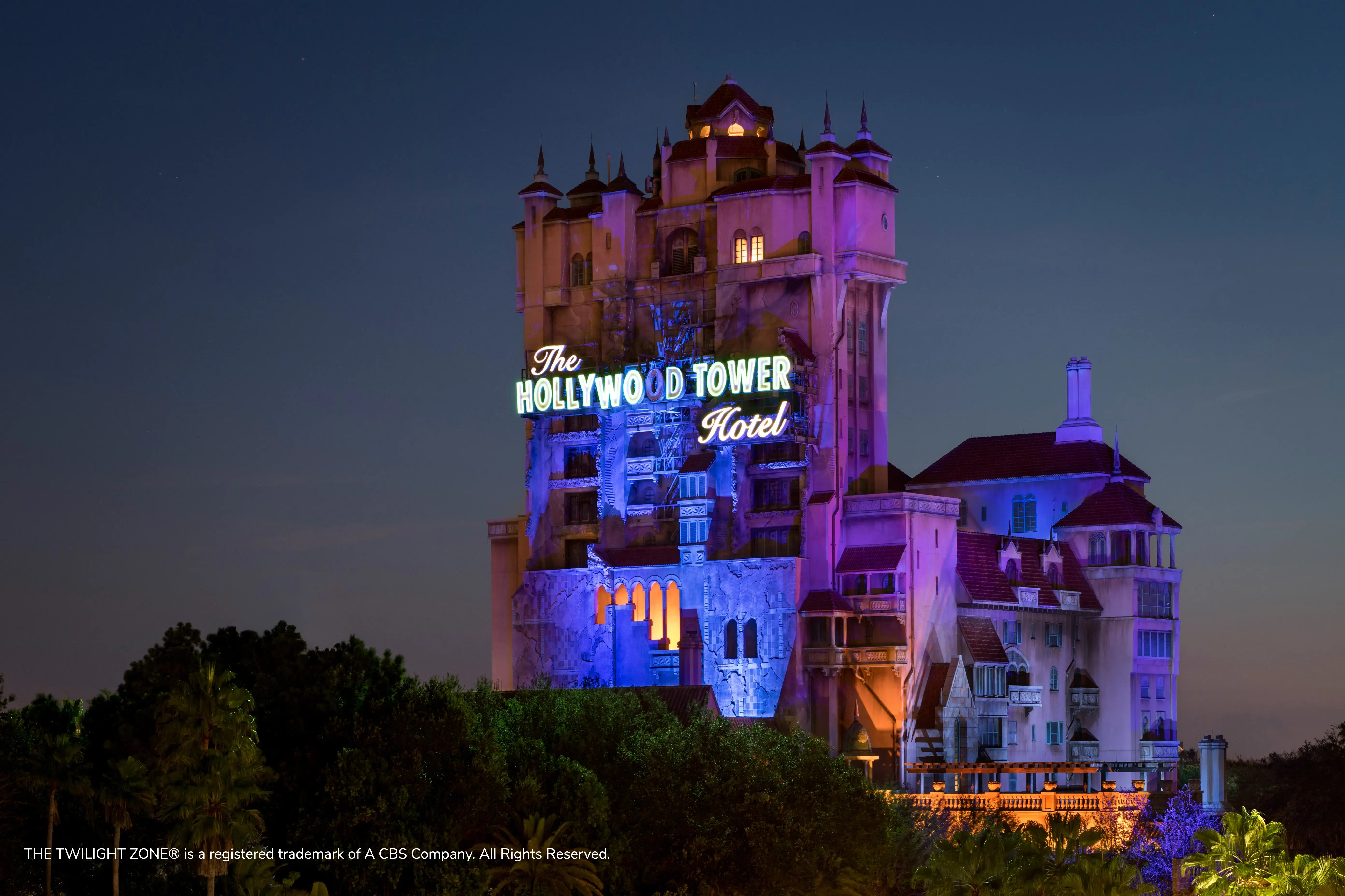 The Hollywood Tower Hotel at Disney lit up at night with text reading THE TWILIGHT ZONE® is a registered trademark of A CBS Company. All Rights Reserved.