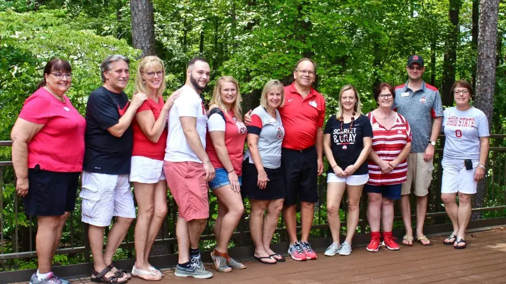ohio state alumni line up for a photo in front of green forestry and bushes