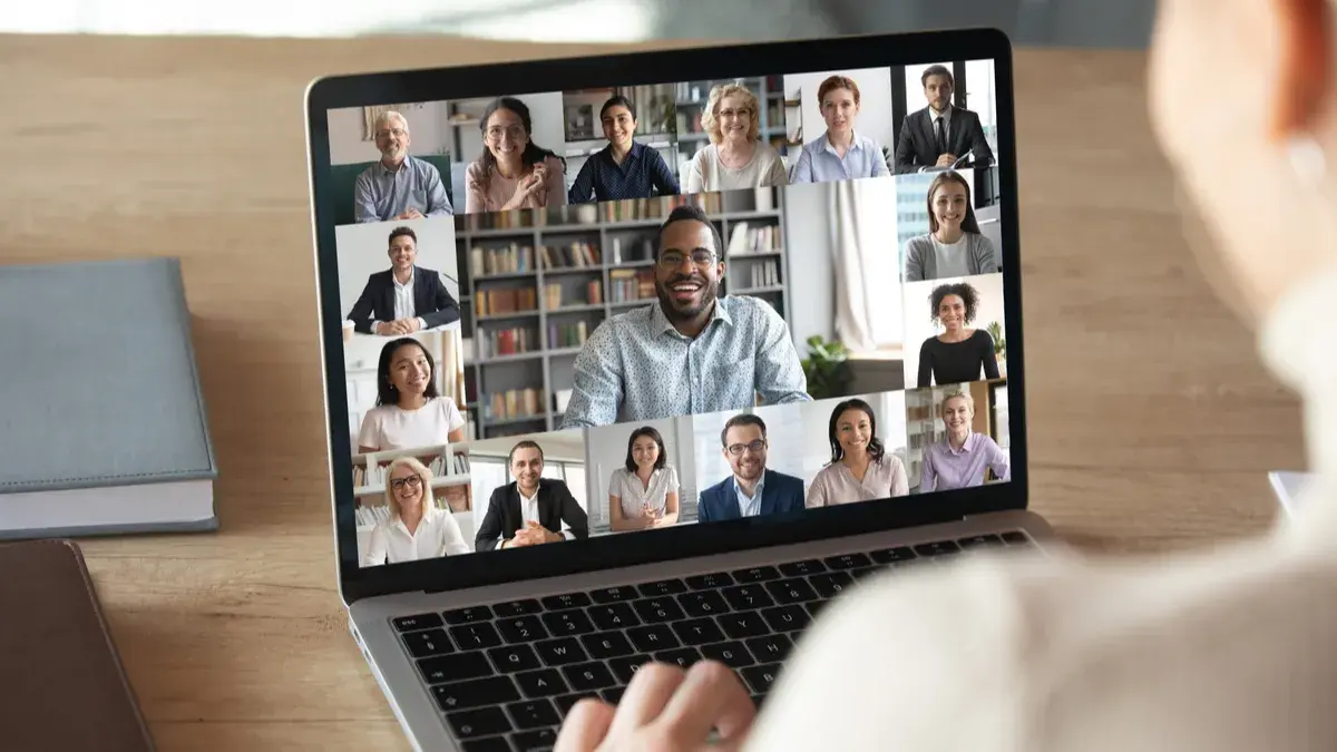 A person working on a laptop with various people and having a virtual meeting