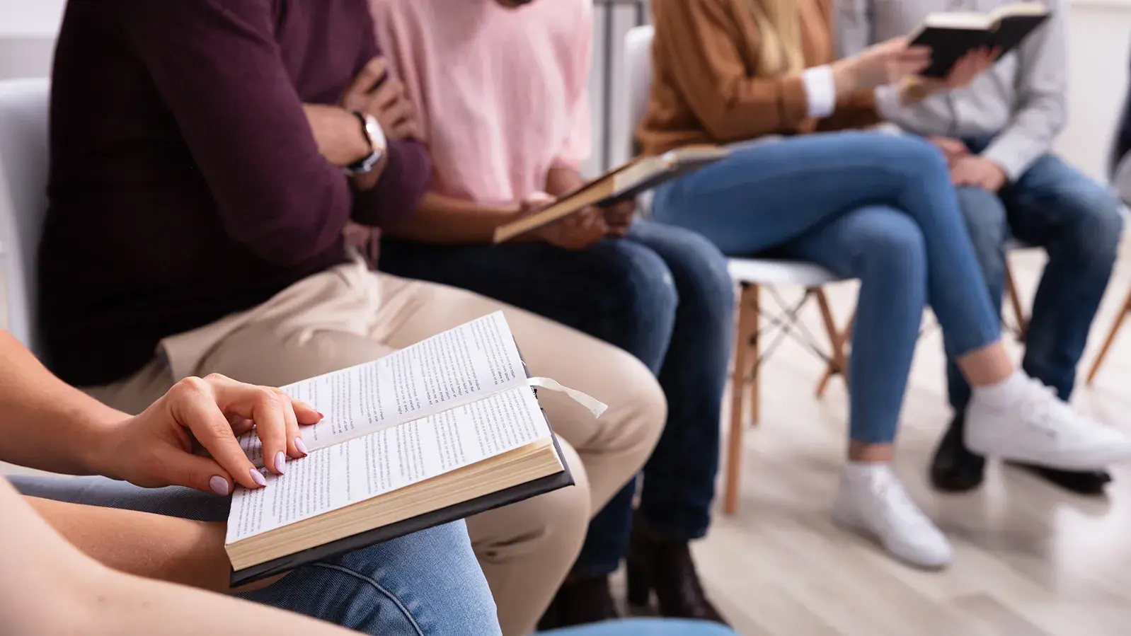 five people gathered together reading from a shared book