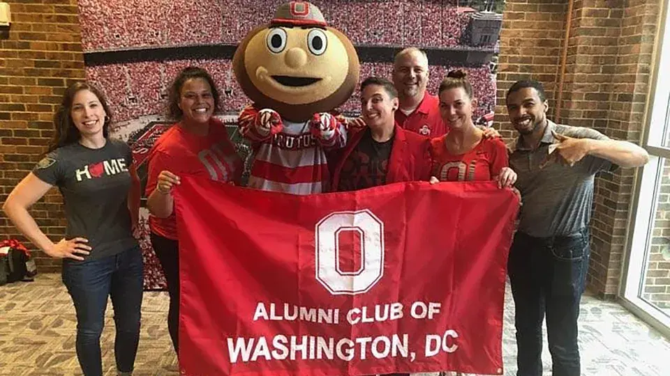six people hold a scarlet flag with the words alumni club of washington, dc printed on it