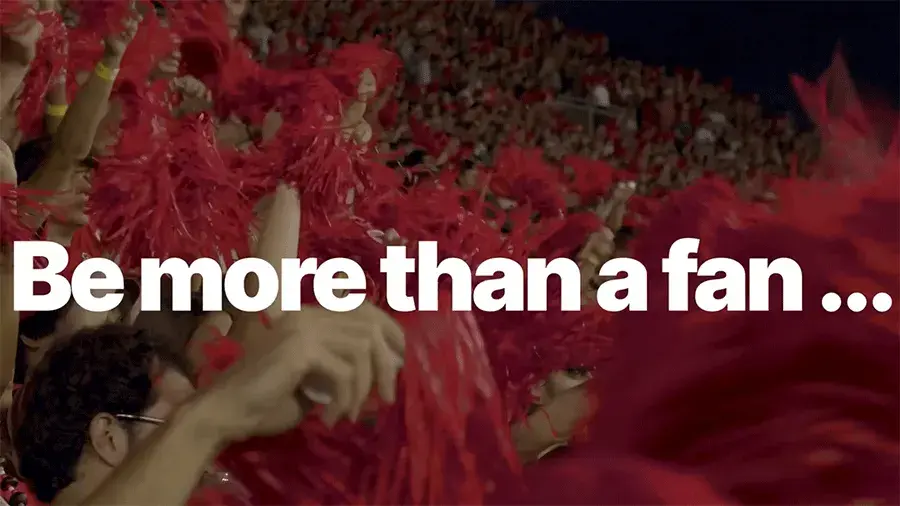 A large crowd of Buckeyes cheering in a stadium with text reading be more than a fan...