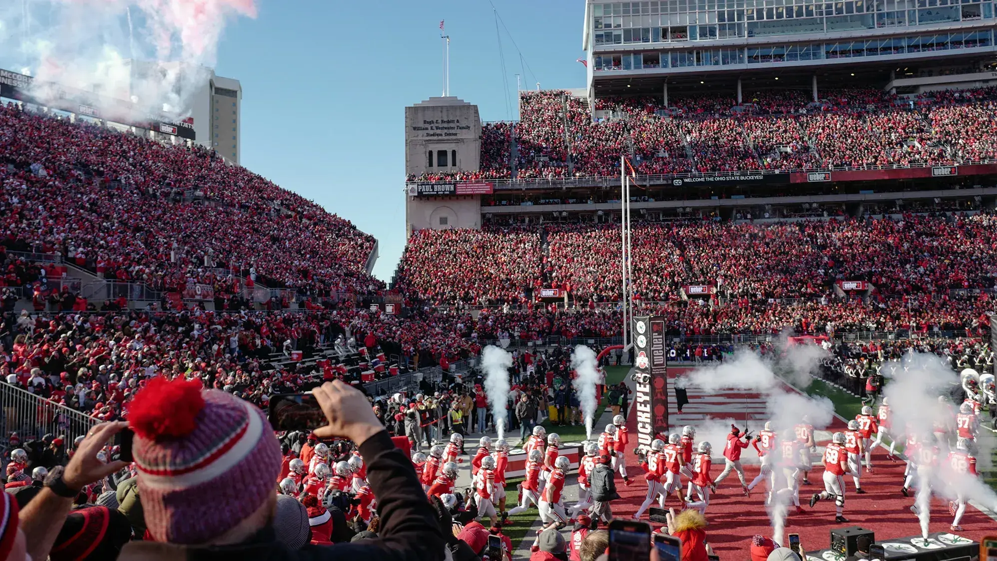 The Ohio State Buckeyes take the field inside Ohio Stadium before a huge crowd. There's a fan in every seat and smoke shoots up as the players come off the ramp